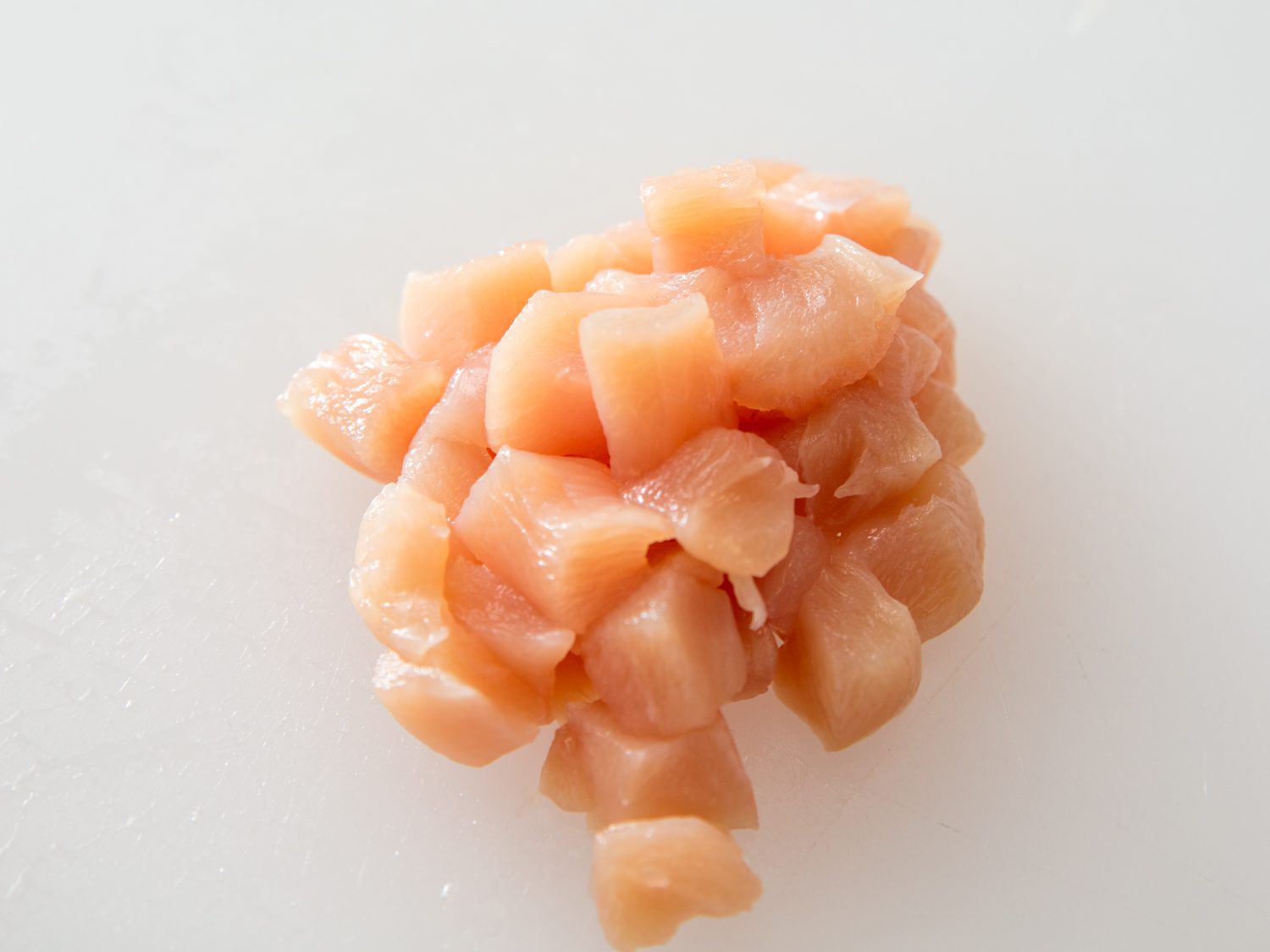 A pile of cubed chicken breast for stir-frying on a cutting board.