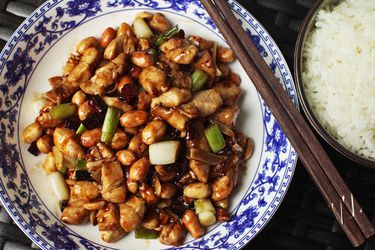 Overhead of kung pao chicken in a bowl with chopsticks next to rice.