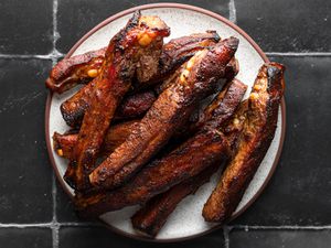 Roasted Chinese spare ribs on a ceramic plate on a black tile background.