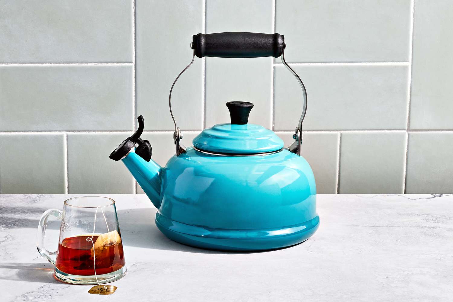 a blue tea kettle on a marble surface with a mug of tea beside it