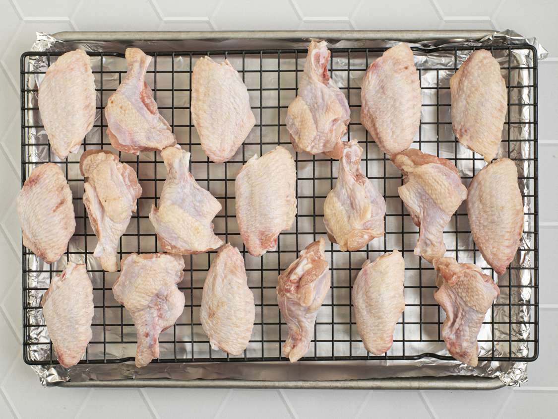 Raw chicken wings tossed with salt and baking soda on a wire rack set inside of a foil-lined rimmed baking sheet.