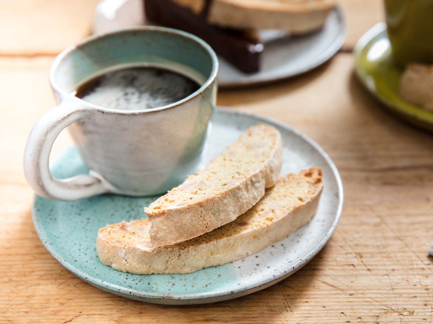 Two biscotti stacked next to a ceramic mug of steaming coffee.