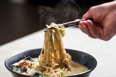 Using chopsticks to pull up the noodles from a bowl of ramen