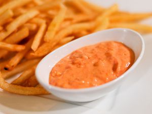一个年代mall dish of sun-dried tomato and roasted garlic mayo next to a plate of French fries.