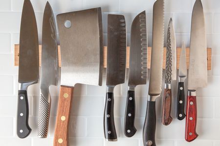 a variety of different knives hanging from a magnetic wooden knife holder