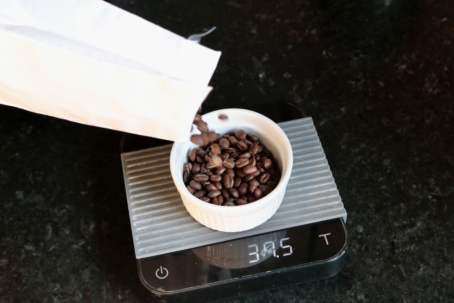 A bag of coffee being poured into a ramekin set on a coffee scale