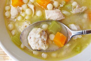 开销汤匙及特写ng up a bite of homemade chickarina soup directly above the bowl.