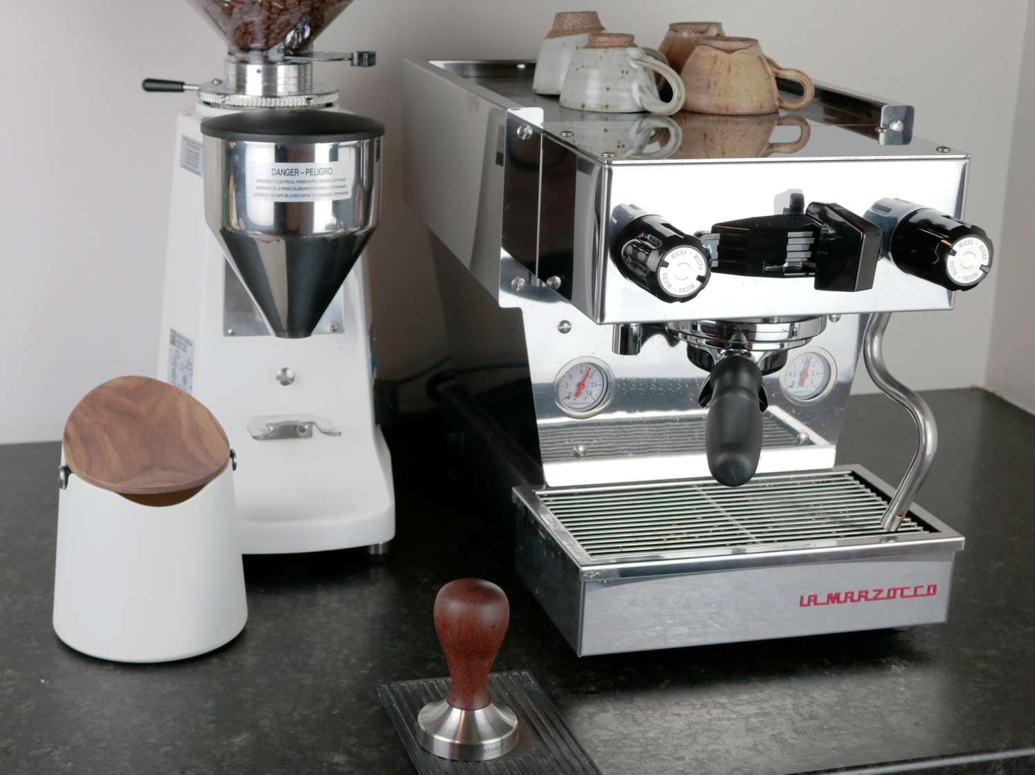 an espresso grinder, espresso machine, knock box and tamper on a counter