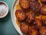 Closeup of a serving platter of fondant potatoes with a ramekin of flaky sea salt on the side.