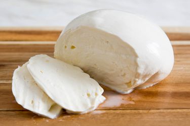 一块切成半片的自制新鲜马苏里拉奶酪球放在木砧板上。