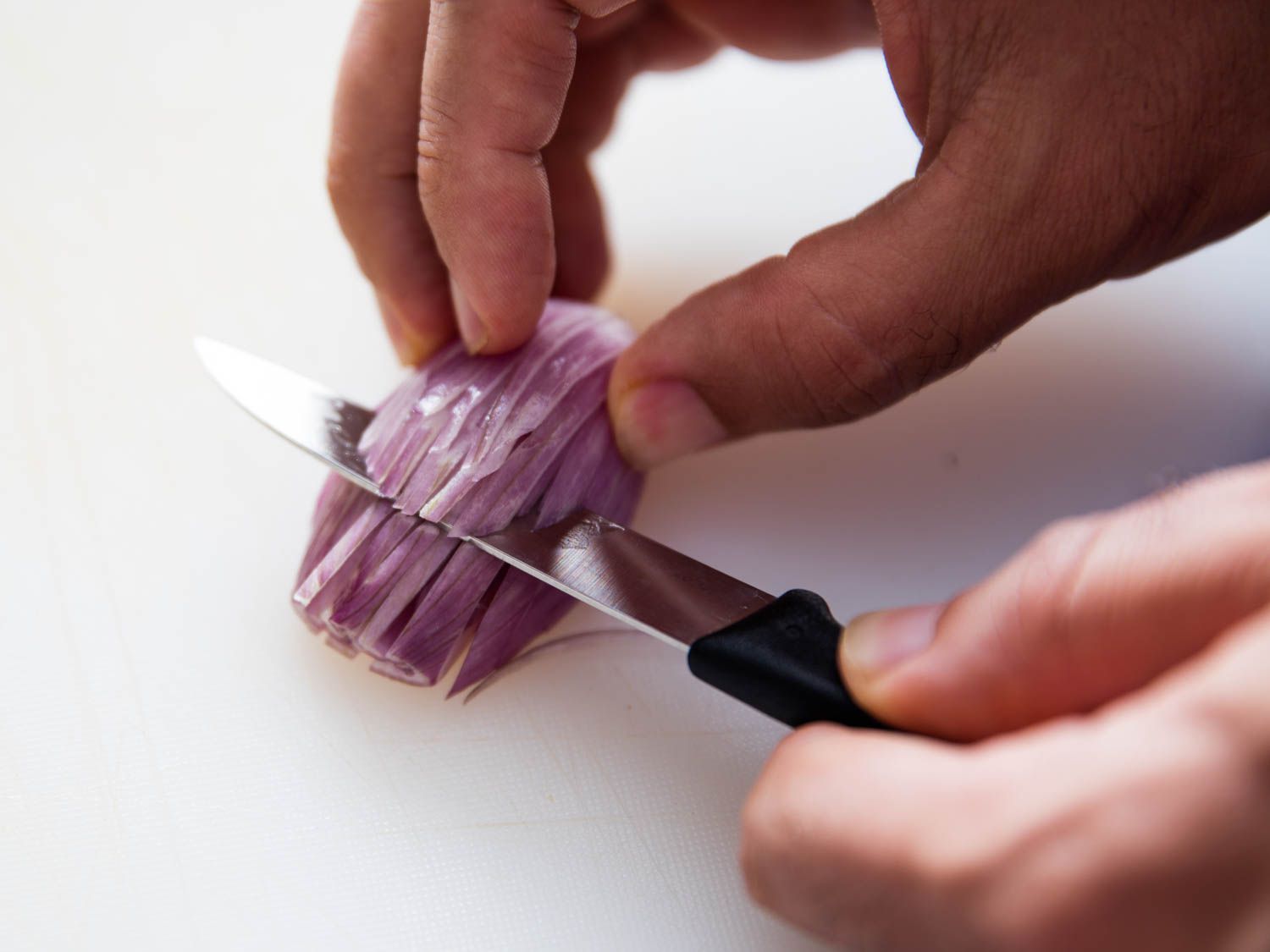 A pairing knife mincing a shallot