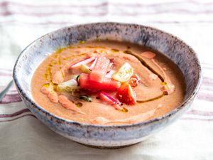 A ceramic bowl of watermelon gazpacho garnished with Calabrian-chili crema, watermelon, and tomatoes.