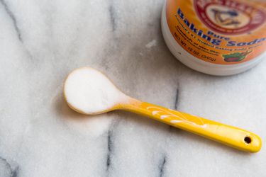 A small spoon holding baking soda with a container of baking soda next to it.