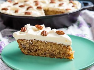 A slice of frosted hummingbird cake baked in a cast iron skillet.