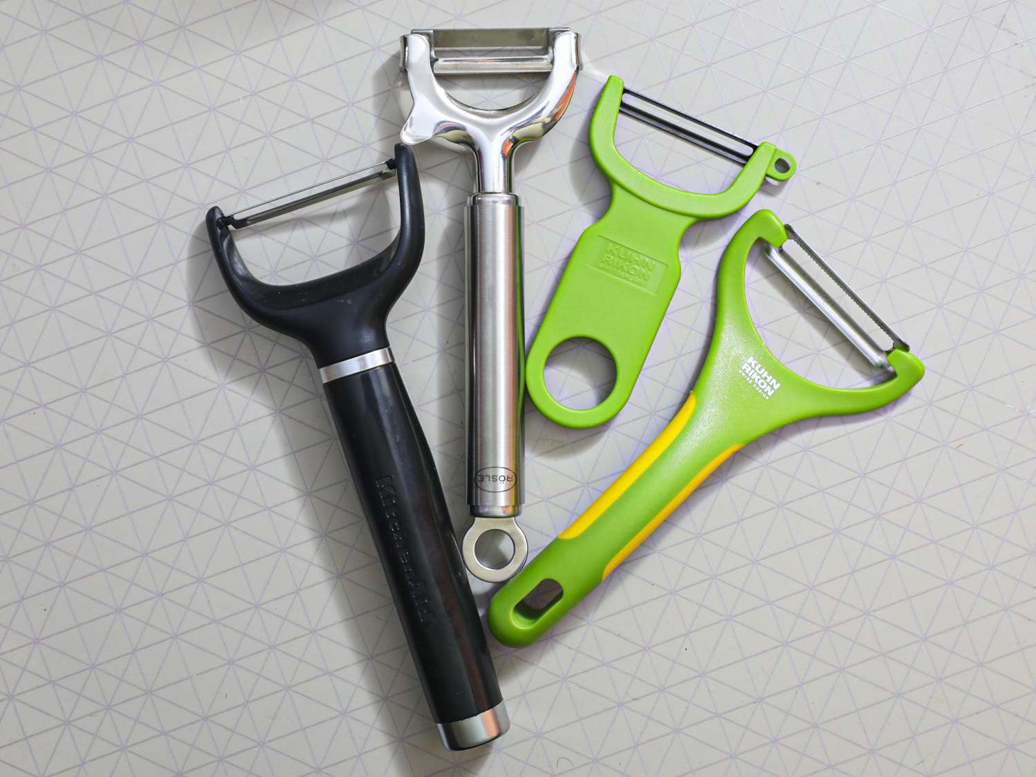 Four vegetable peelers on a grey surface