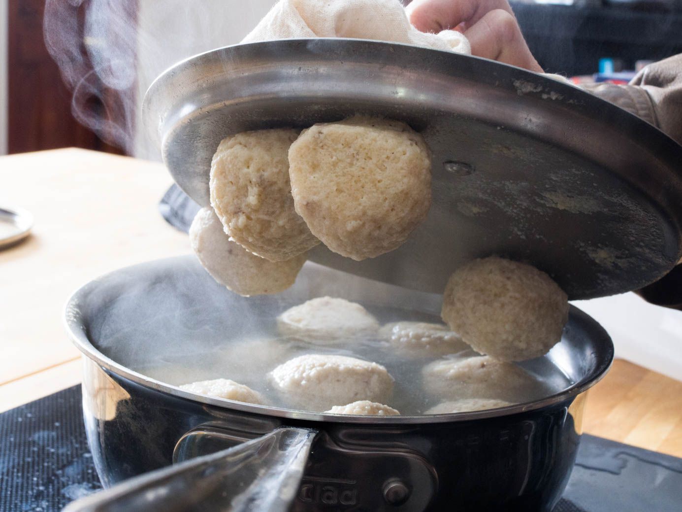 Author removing lid from a pan of poaching matzo balls. 4 of the balls are stuck to the lid.
