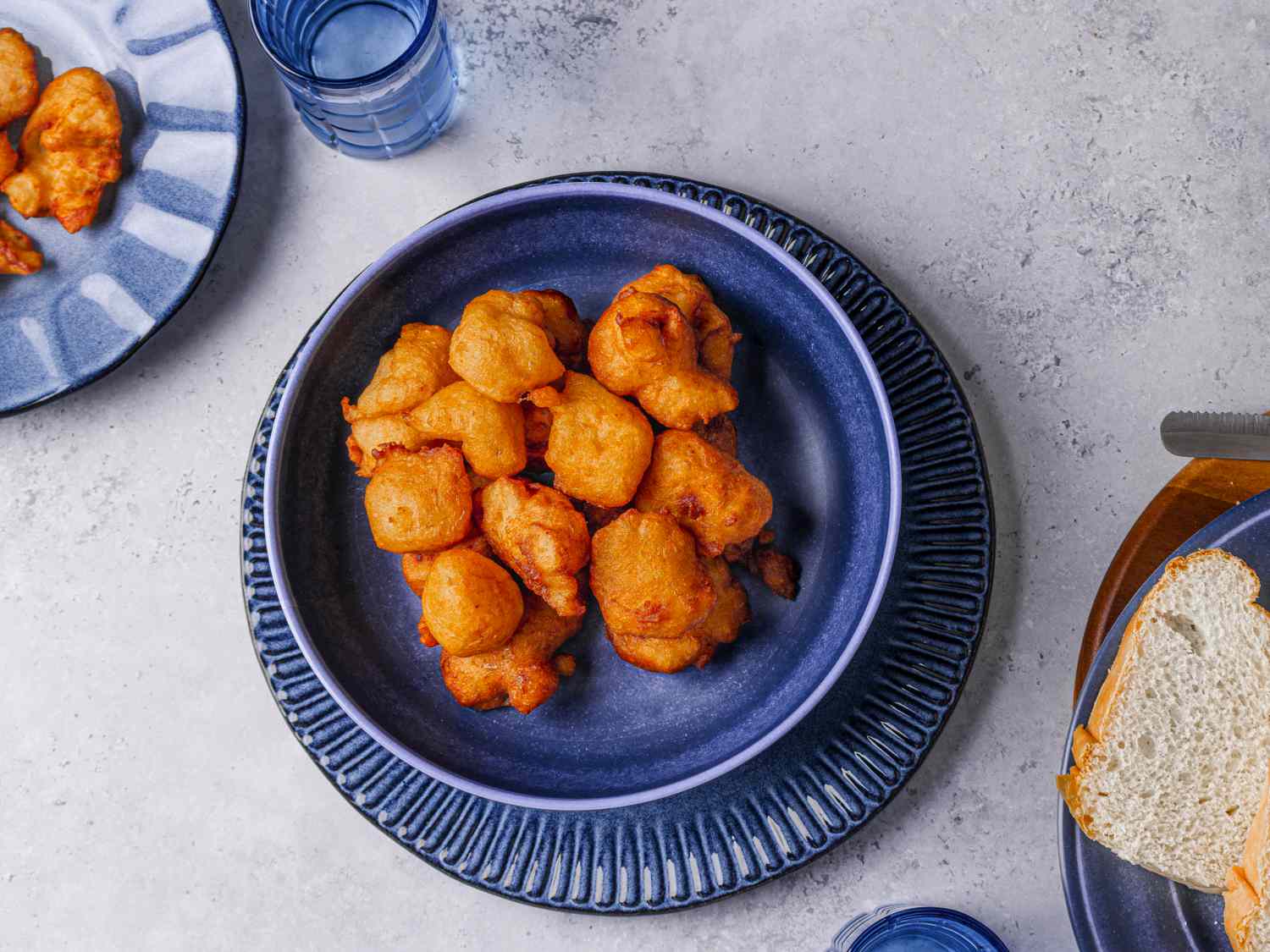 Akara piled on a dark blue bowl next to a plate of white bread and a smaller server plate with akara.