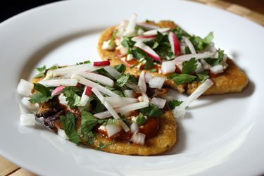 Huaraches with Black Beans and Radishes on a white plate.