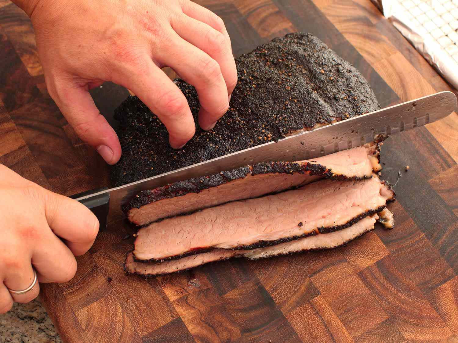 Hands cutting a finished brisket into slices on a wooden cutting board. This brisket does not have a smoke ring.