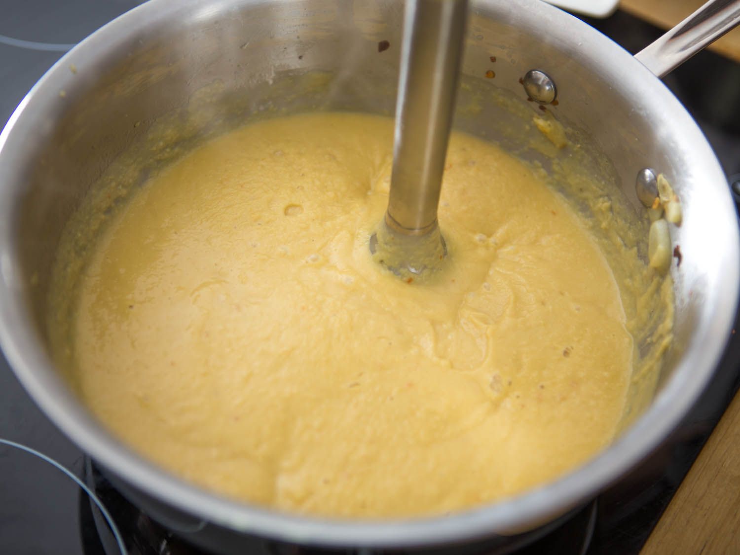 用浸入式搅拌机将鹰嘴豆放入锅中搅拌。