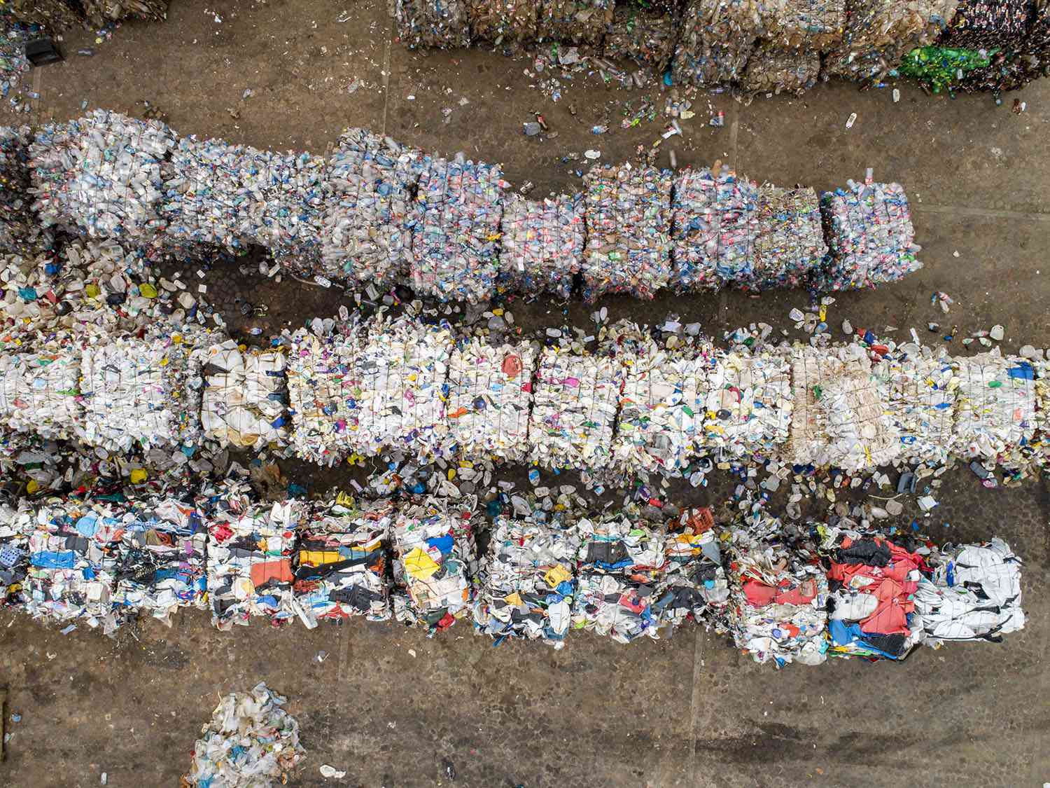 Straight down aerial view of compressed and tied up blocks of various plastic items and plastic bottles awaiting recycling at a recycling center