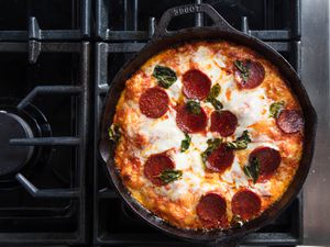 Overhead view of a pan pizza topped with pepperoni and torn basil leaves.