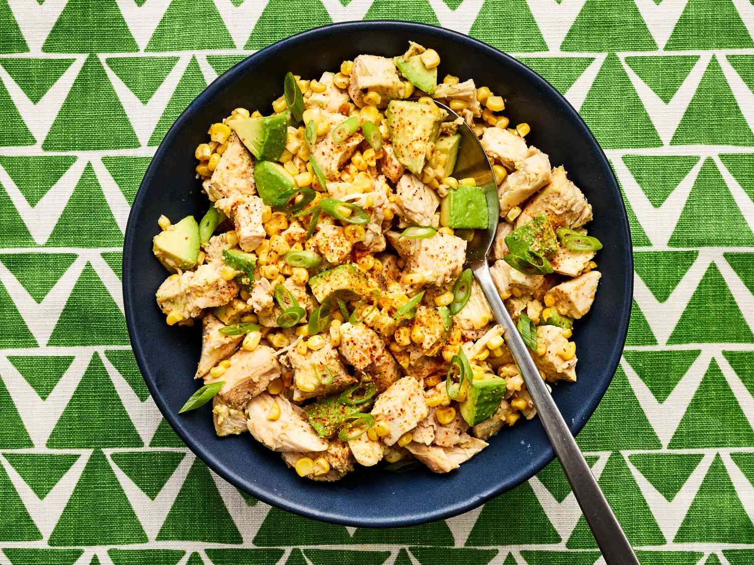 Overhead view of avocado and chicken salad on a green triangle patterned backdrop
