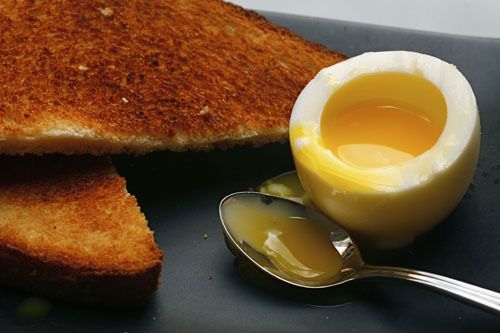 一颗半熟的鸡蛋，切开露出溏心的蛋黄，旁边是一片吐司和一把勺子。gydF4y2Ba