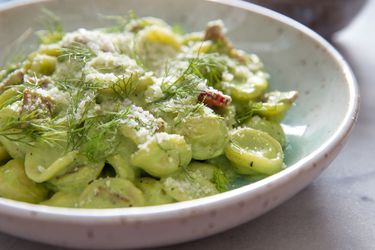 A bowl of pasta with a creamy, pale green sauce, garnished with fresh fennel fronds.