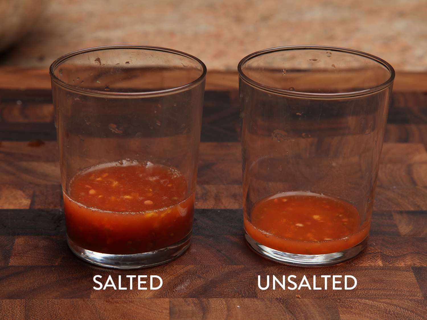 Two glasses showing the respective amounts of liquid drained from tomatoes that have been salted versus unsalted tomatoes