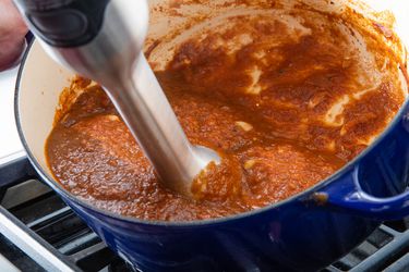 Blending sauce for butter chicken with an immersion blender in an enamel cast iron Dutch oven.