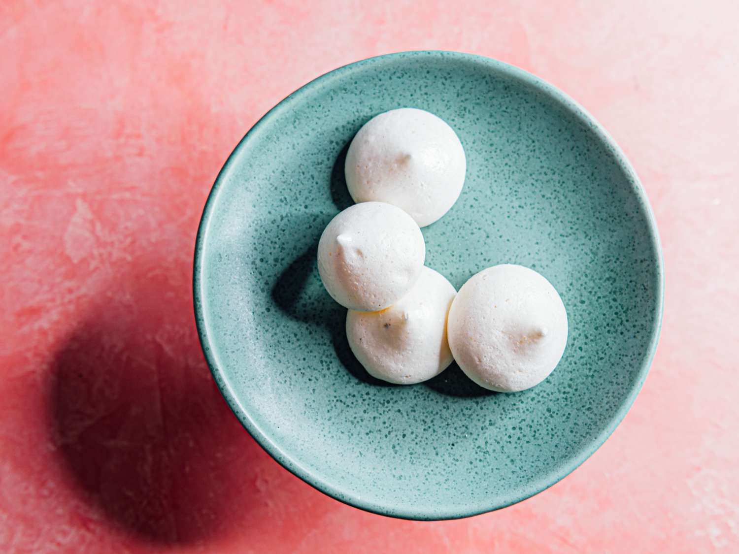 aquafaba-cardamom meringue cookies on a blue plate on a pink background