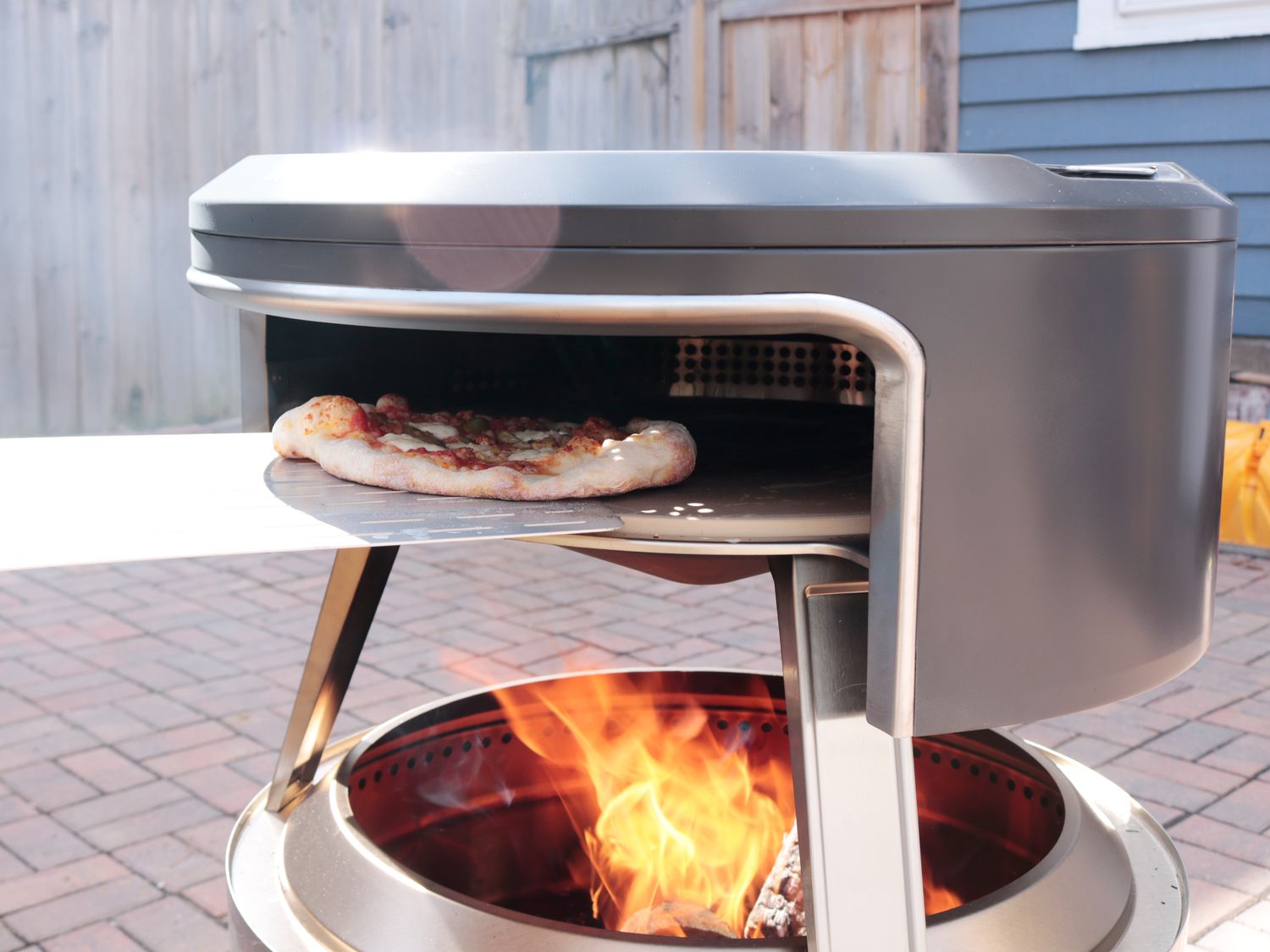 a pizza cooking in an outdoor pizza oven that fits over a fire pit