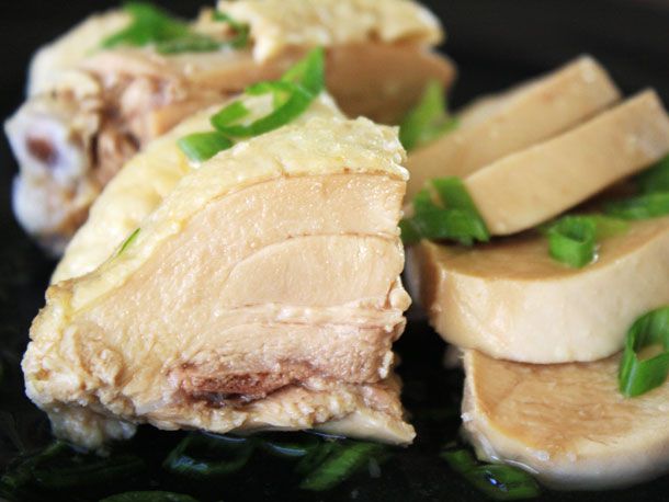 Poached chicken cut up into pieces, garnished with sliced scallions.