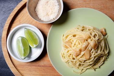 Overhead view of a plate of garlic pasta with grated cheese and lime wedges alongside