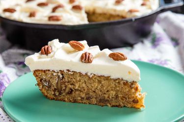 A slice of frosted hummingbird cake baked in a cast iron skillet.