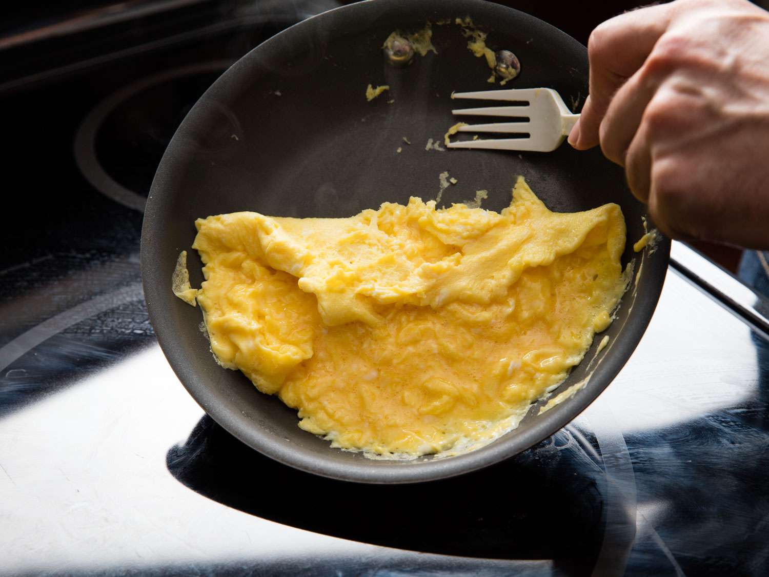 Using a plastic fork to roll the edge of scrambled eggs with large curds toward the center of a nonstick skillet