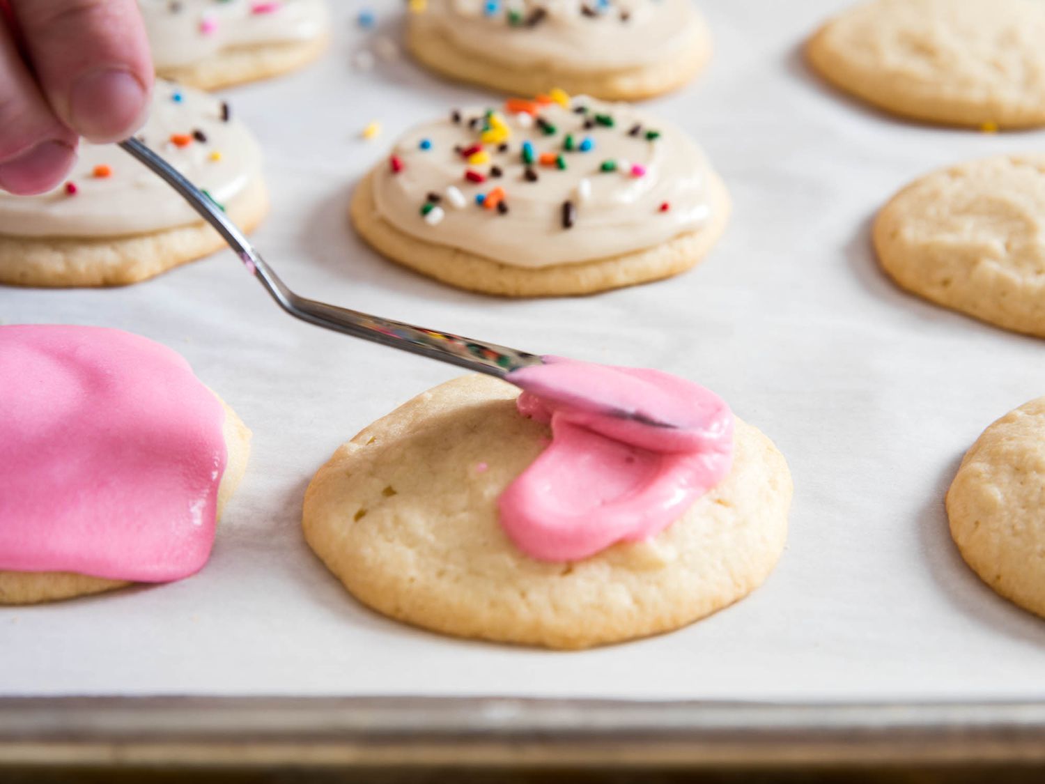 Closeup of spreading pink icing on sugar cookie.