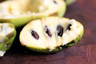 A pawpaw fruit cut in half and resting on a cutting board