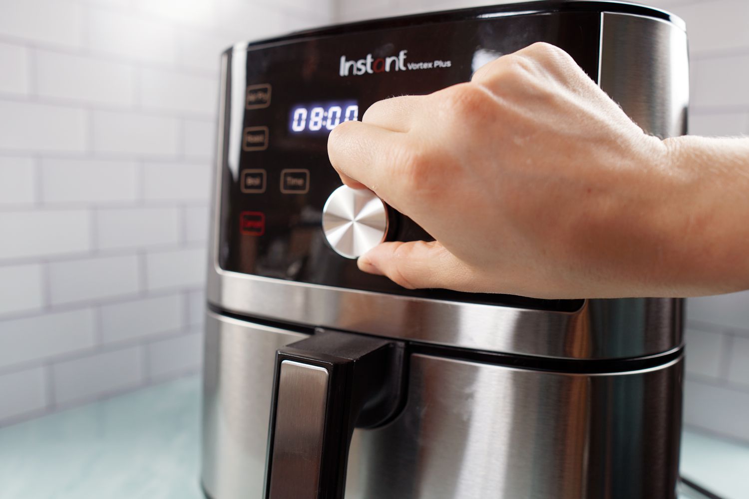 A hand using an air fryer's control knob to change the cooking time