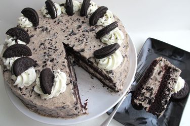 Chocolate Oreo cake on a cake stand with a slice removed and placed on a black plate.