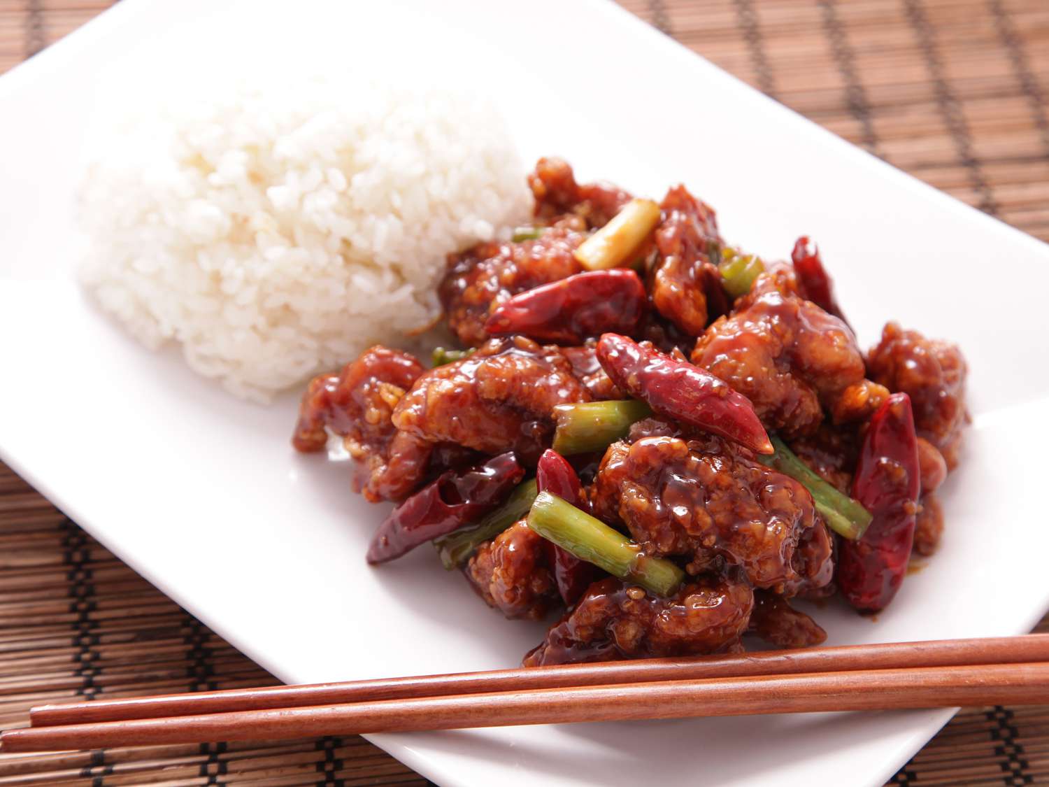 General Tso's Chicken on a rectangular white plate with white rice and a pair of chopsticks.
