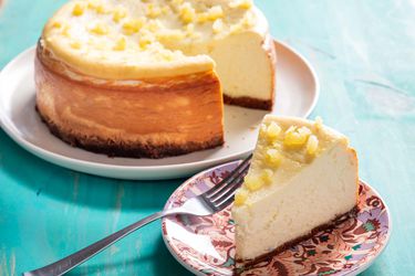 A slice of lemon ricotta cheesecake plated next to the whole cake.