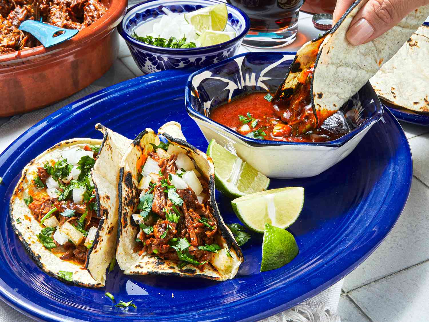 Side view of dipping birria tacos into consome