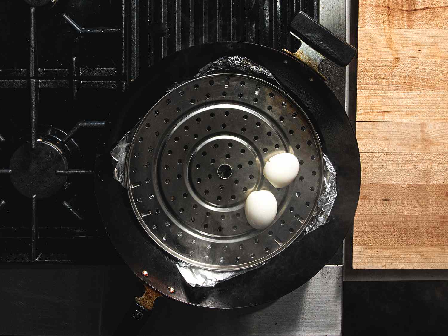 俯视两个鸡蛋坐在一个穿孔的架子上锡箔内衬锅，准备被熏制。