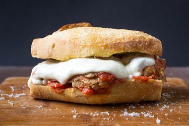Profile view of an Italian-American meatball sandwich, served on a small wooden cutting board.