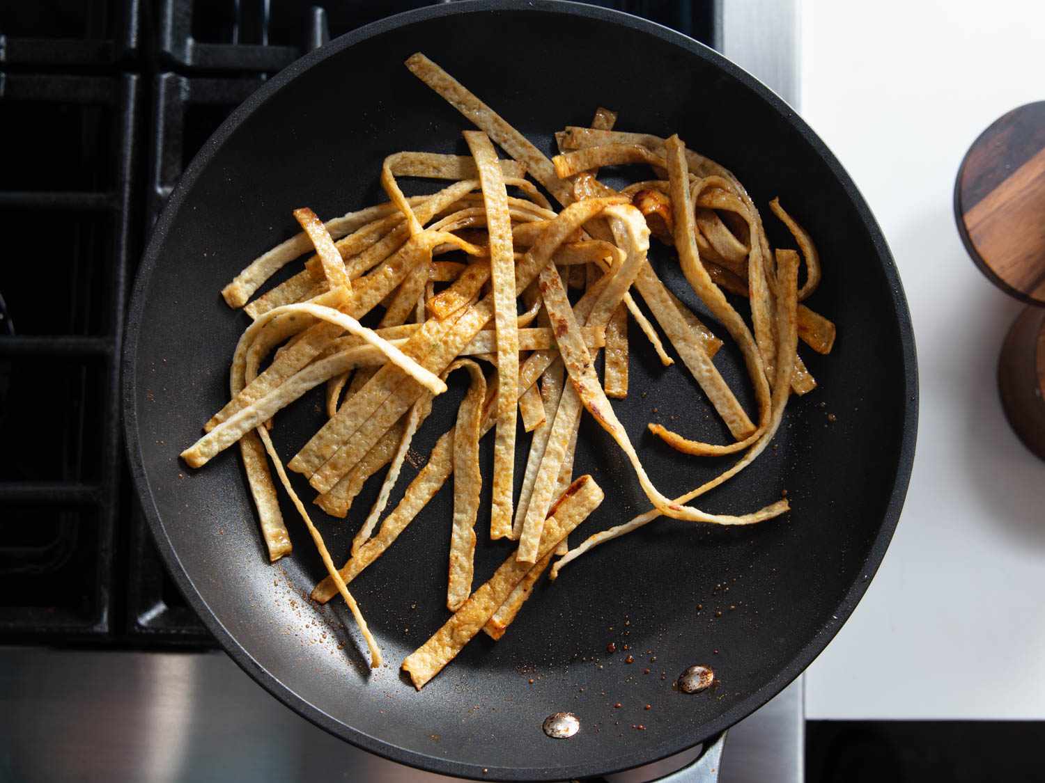 Overhead shot of long and skinny strips of Korean fishcake frying in a nonstick pan.