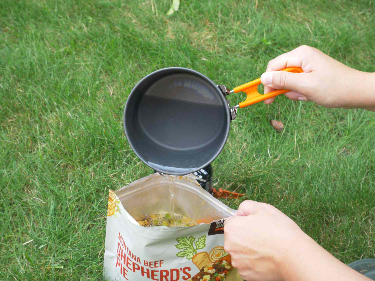 pouring water from a small backpacking pot into a pouch of backpacking food