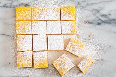 Overhead image showing sliced lemon bar squares topped with powdered sugar on a marble countertop.