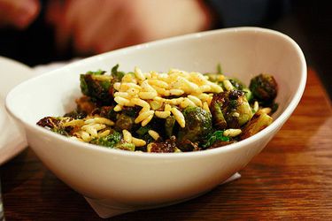 一个白色的椭圆形碗of Momofuku Brussels sprouts topped with puffed rice.